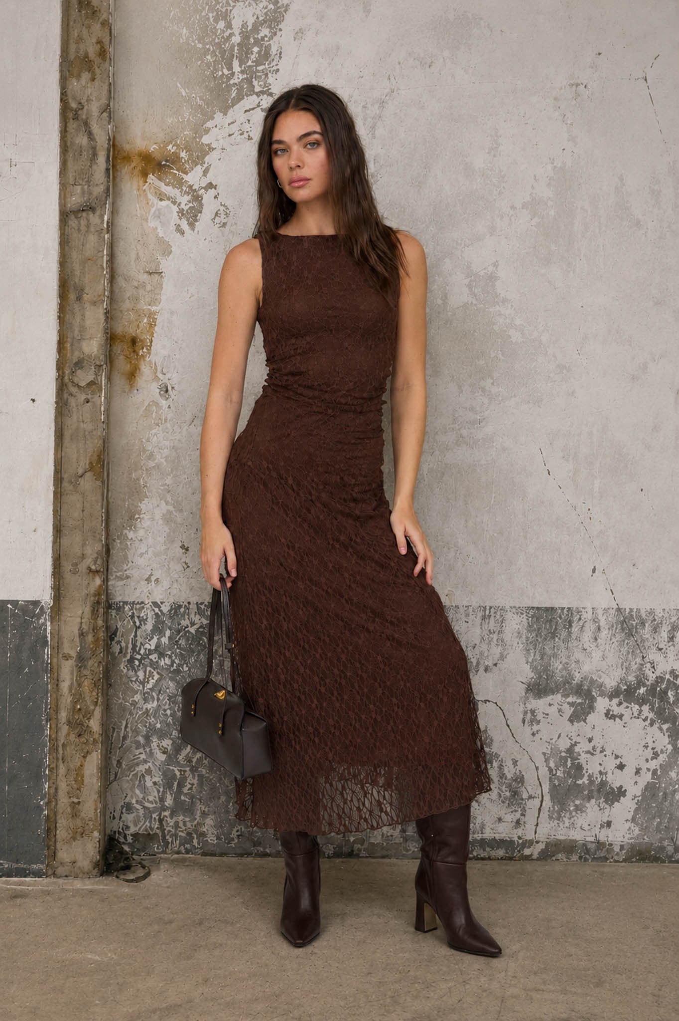 Woman wearing a brown dress standing against a textured wall.