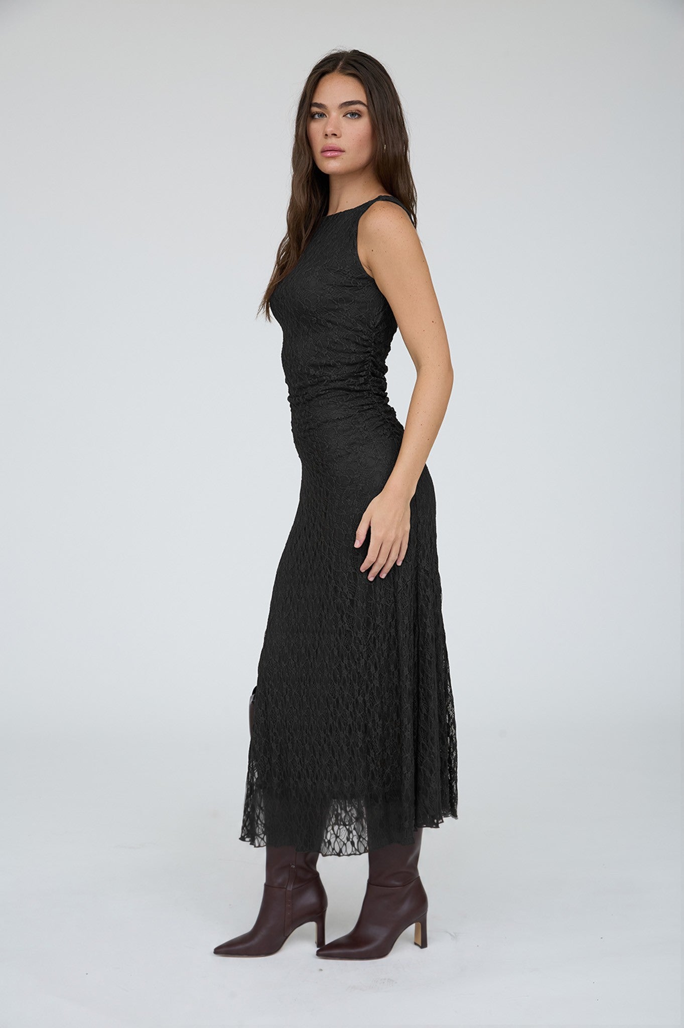 Woman wearing a black lace dress with maroon boots on a white background