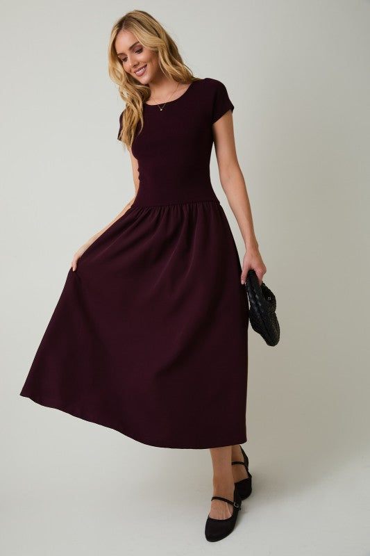 Woman wearing a burgundy dress holding a black clutch against a plain background