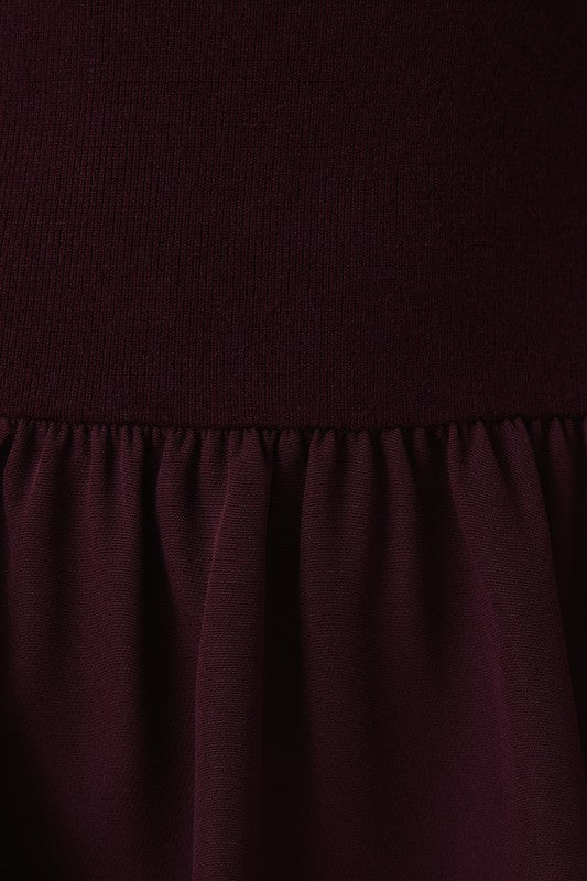 Close-up of a dark burgundy dress showing the ribbed knit texture of the bodice and the draped fabric of the skirt.
