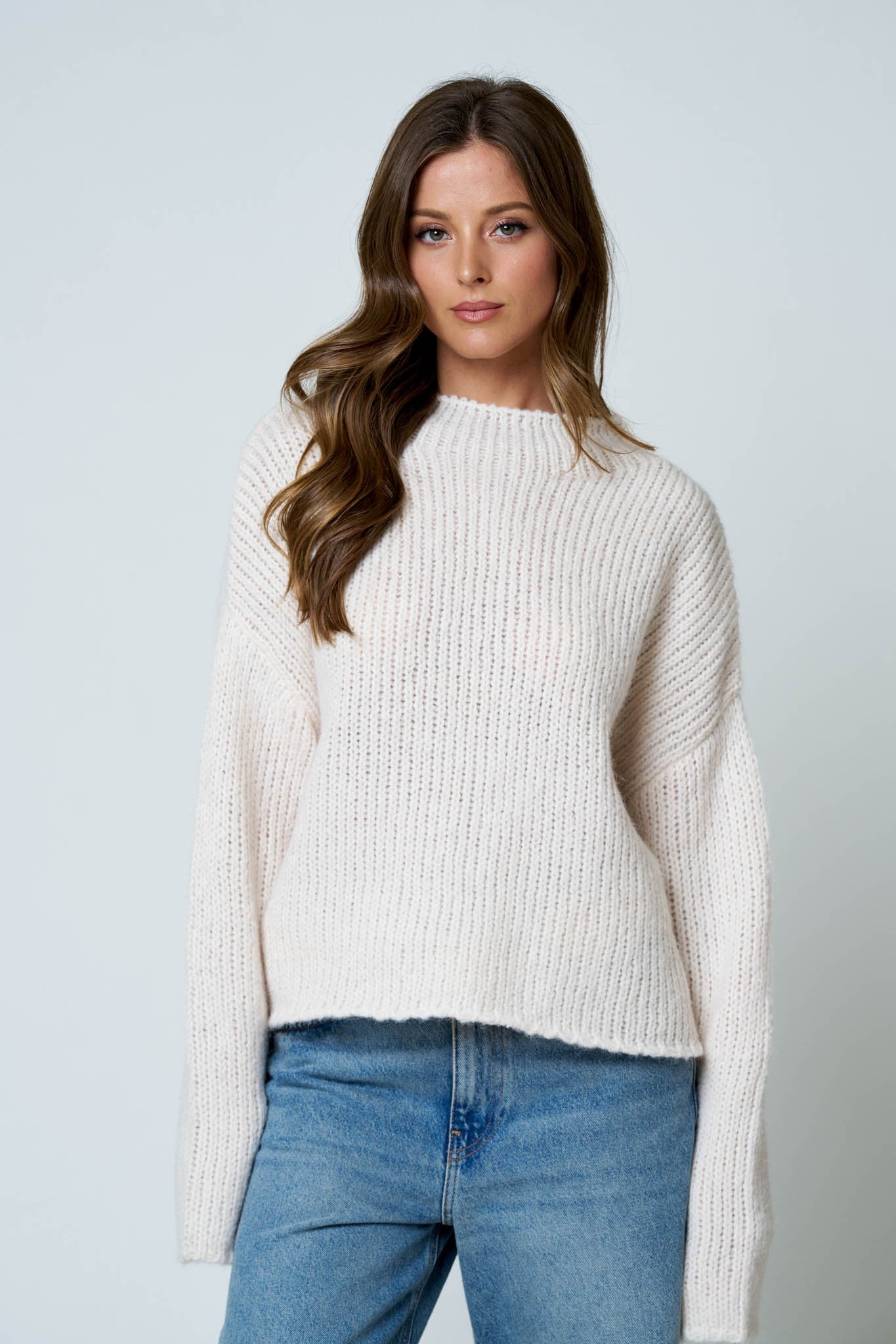 Woman wearing a white sweater and blue jeans against a light gray background