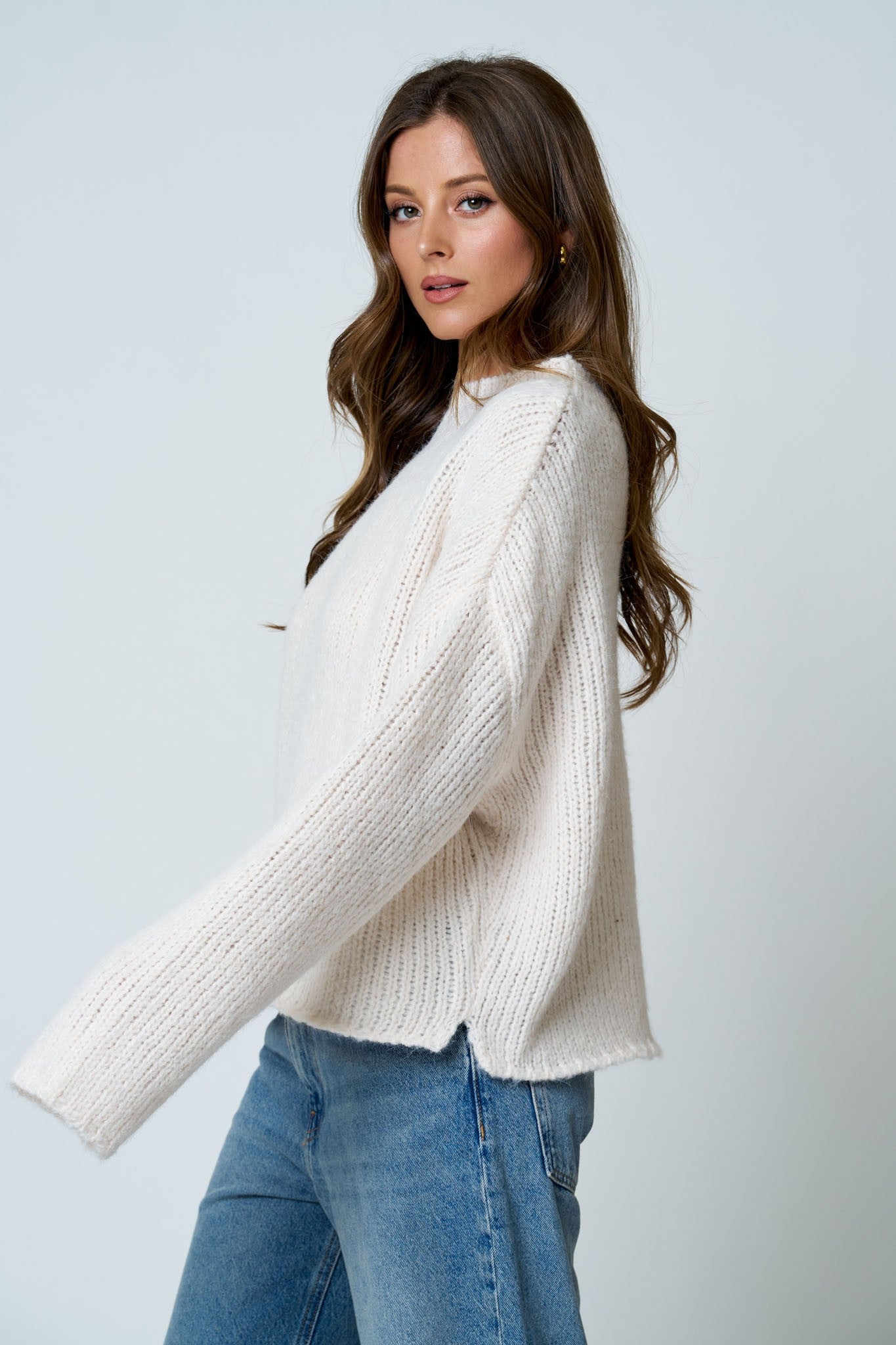Woman wearing a cream sweater and blue jeans against a white background