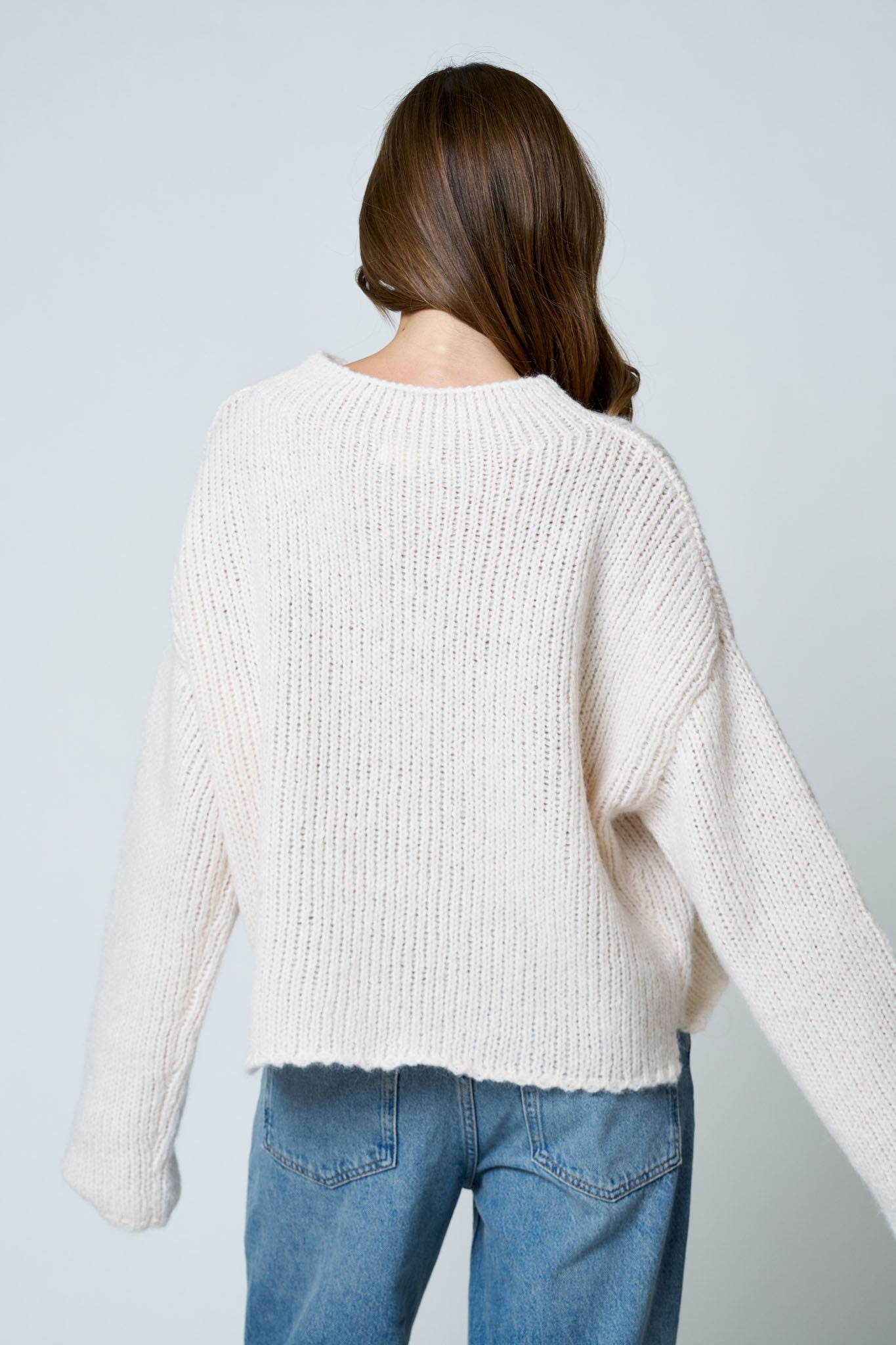 Person wearing a white sweater and blue jeans against a light gray background