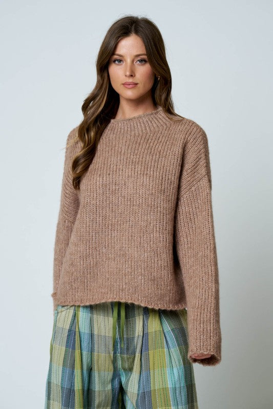 Woman wearing a brown knitted sweater and plaid pants on a light gray background