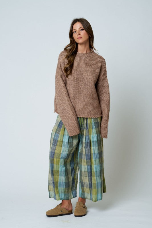 Woman wearing a brown sweater and plaid pants on a white background
