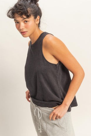 Person wearing a black sleeveless top and gray pants on a plain background