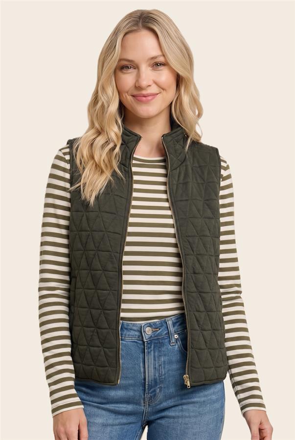 A woman wearing an olive green quilted zip-front vest over a beige and olive striped long-sleeve shirt with blue jeans, photographed against a plain light beige studio background.