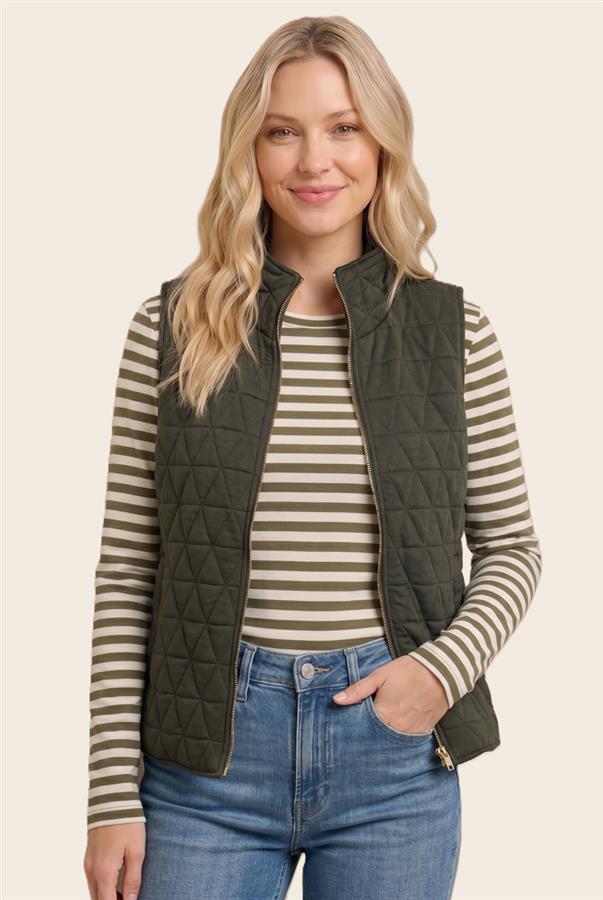 A woman wearing an olive green quilted zip-front vest over a beige and olive striped long-sleeve top, paired with blue jeans, against a plain light beige studio background.