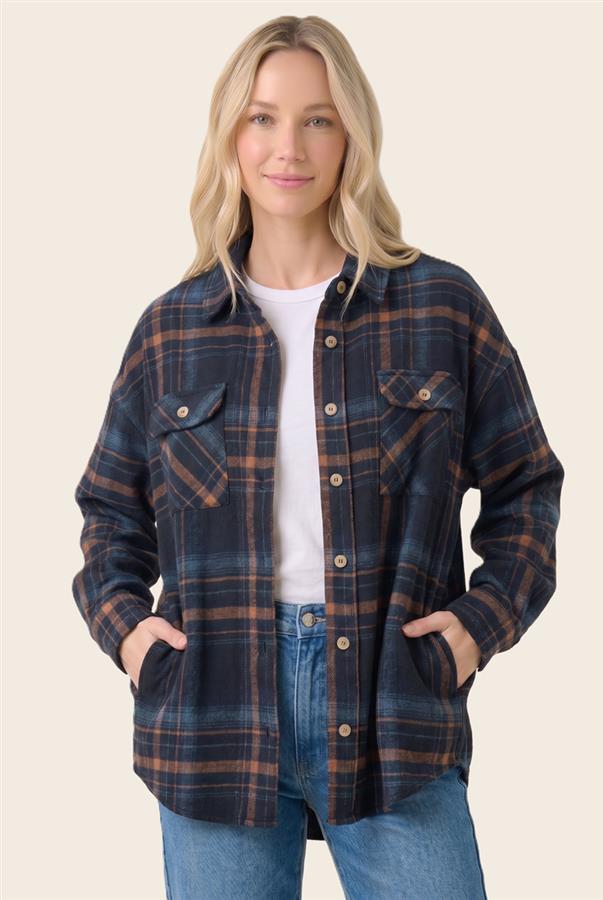 A woman wearing a navy blue and brown plaid button-up flannel shirt over a white t-shirt and blue jeans, standing against a solid light beige background.