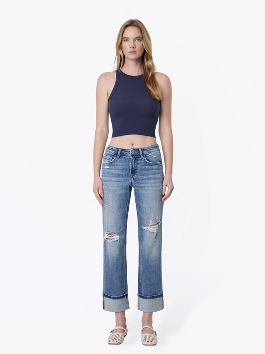 A woman modeling a sleeveless navy blue crop top and light-wash blue distressed jeans with cuffed hems, paired with beige woven sandals, against a plain white studio background.