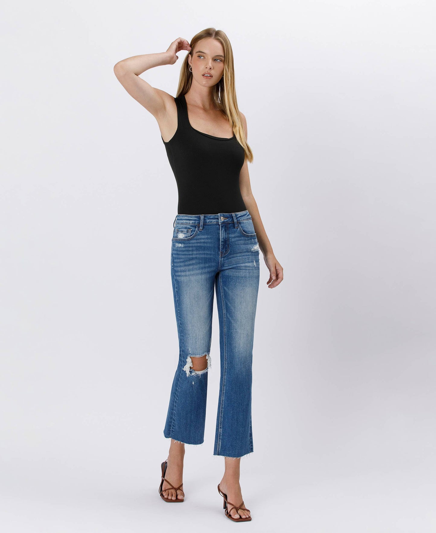 Woman wearing a black tank top and blue jeans on a white background