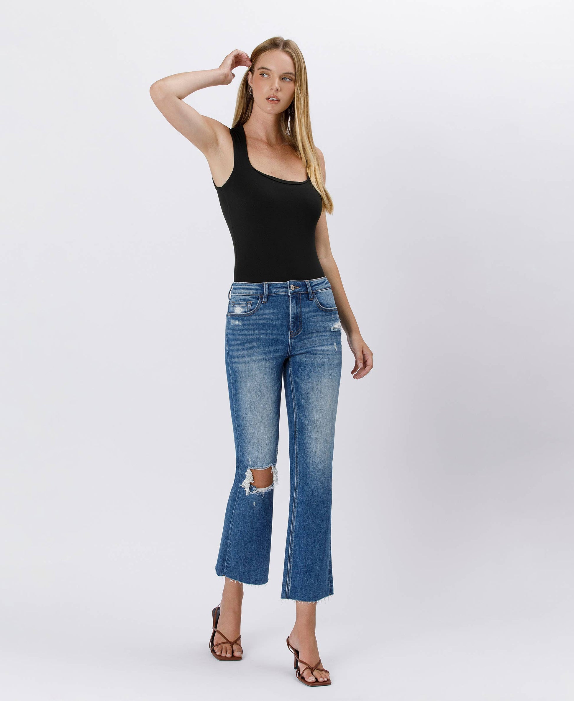 Woman wearing a black tank top and blue jeans on a white background