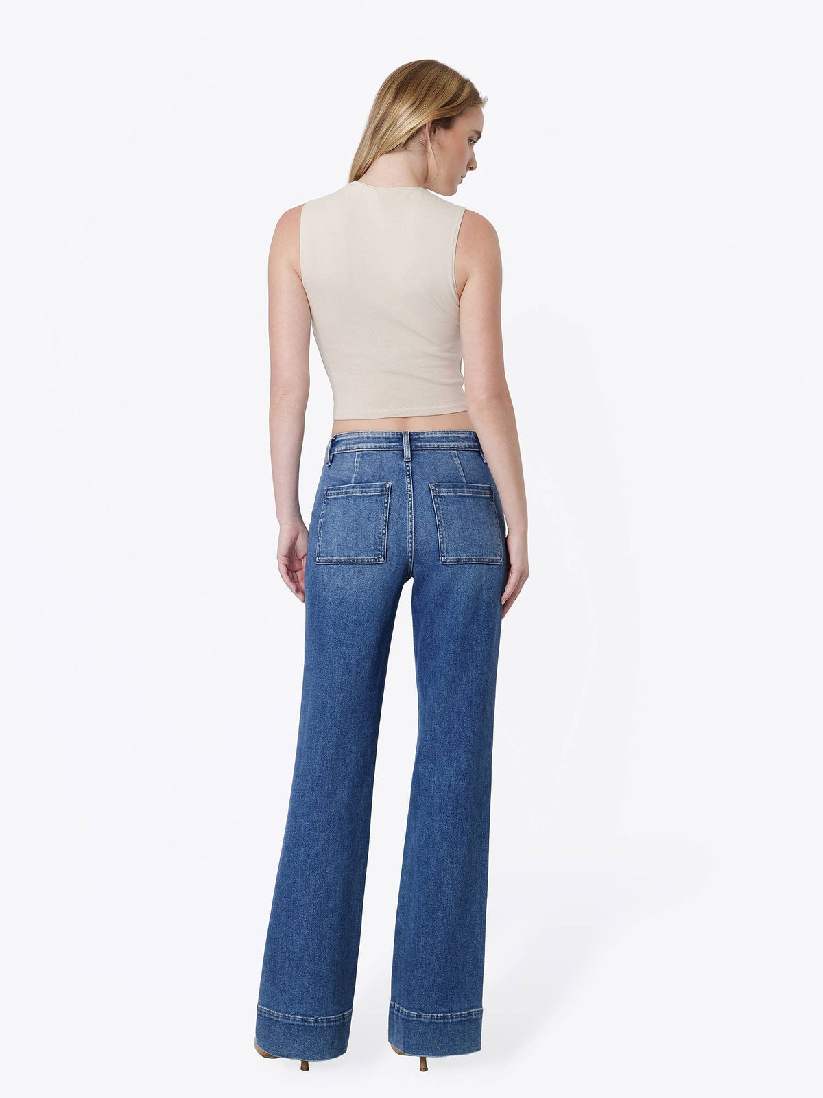 A woman shown from the back wearing a beige sleeveless crop top and blue wide-leg jeans against a plain white studio background.