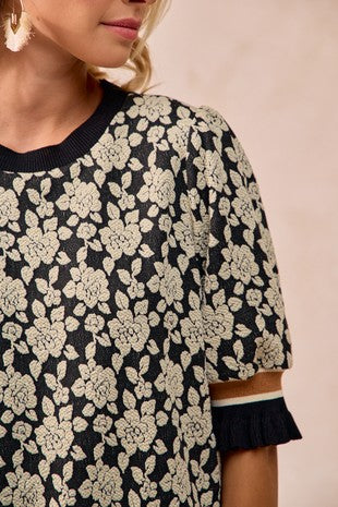 Close-up of a person wearing a black floral patterned dress with a plain background