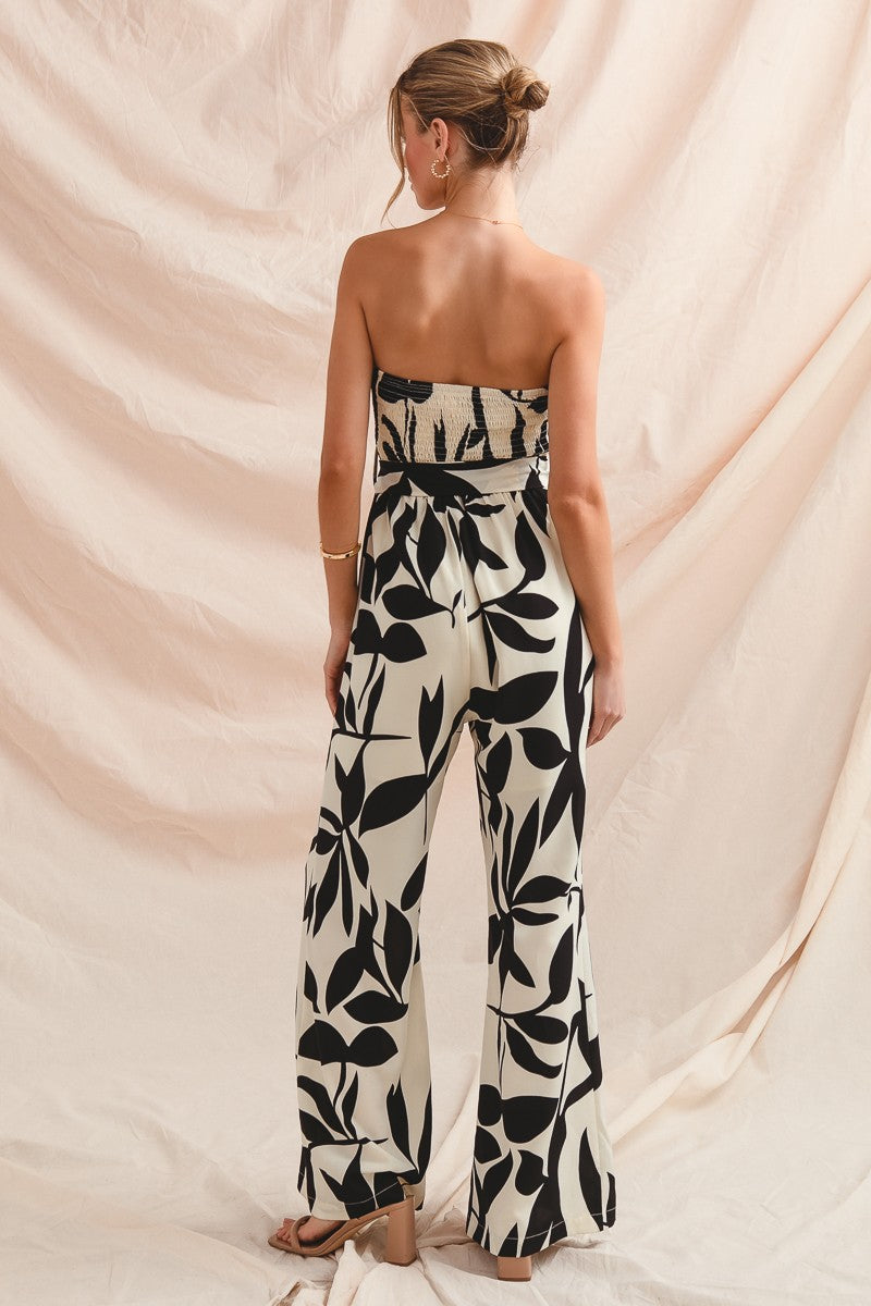 Woman wearing a strapless jumpsuit with black leaf pattern against a beige backdrop