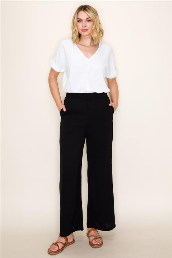 Woman wearing a white top and black pants against a beige background