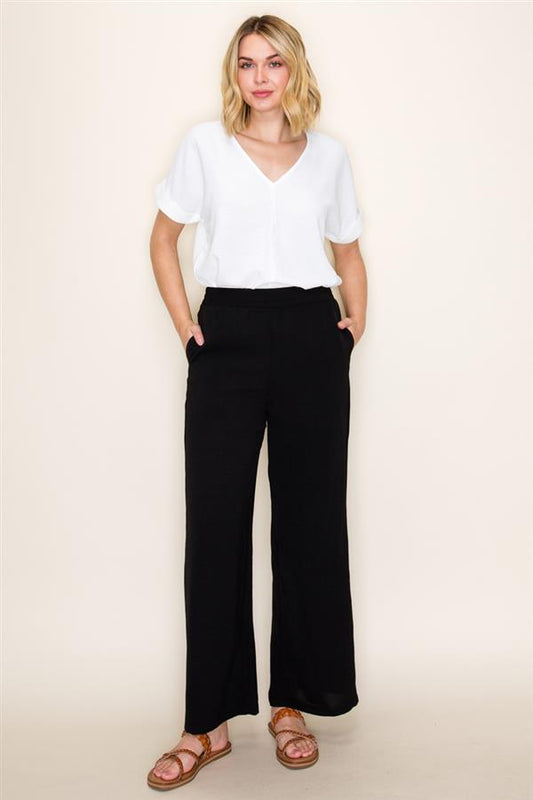 Woman wearing a white top and black pants against a beige background