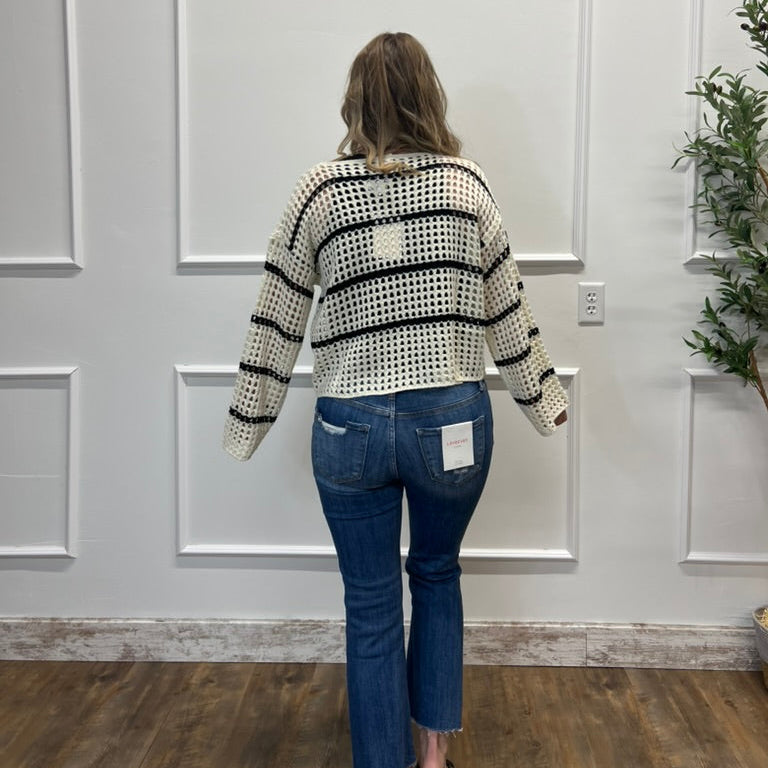 Person wearing a black and white patterned sweater and blue jeans standing in front of a white paneled wall.
