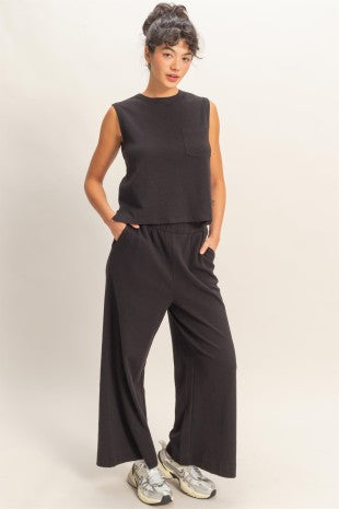 Woman wearing a black sleeveless top and wide-leg pants on a plain background