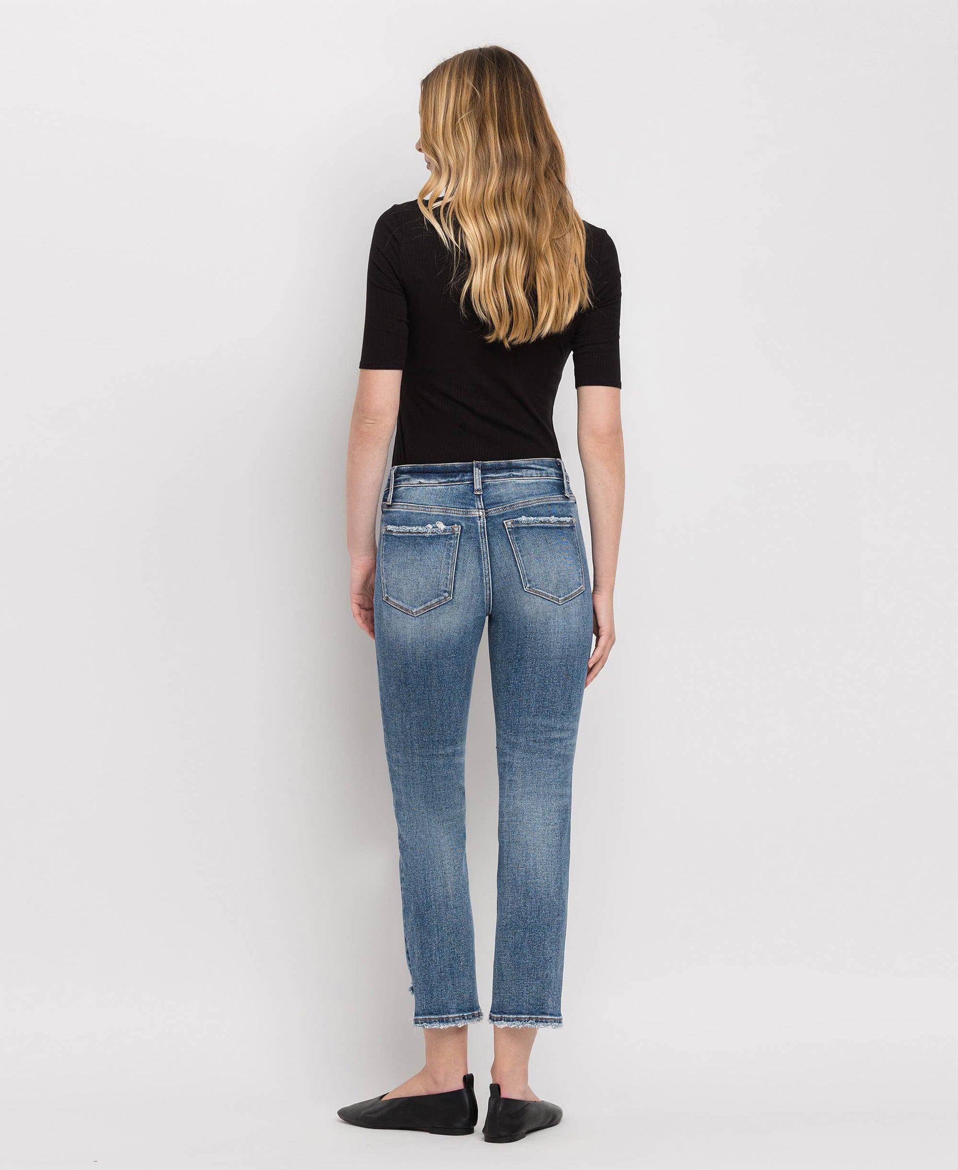 Woman wearing blue jeans and a black top on a white background