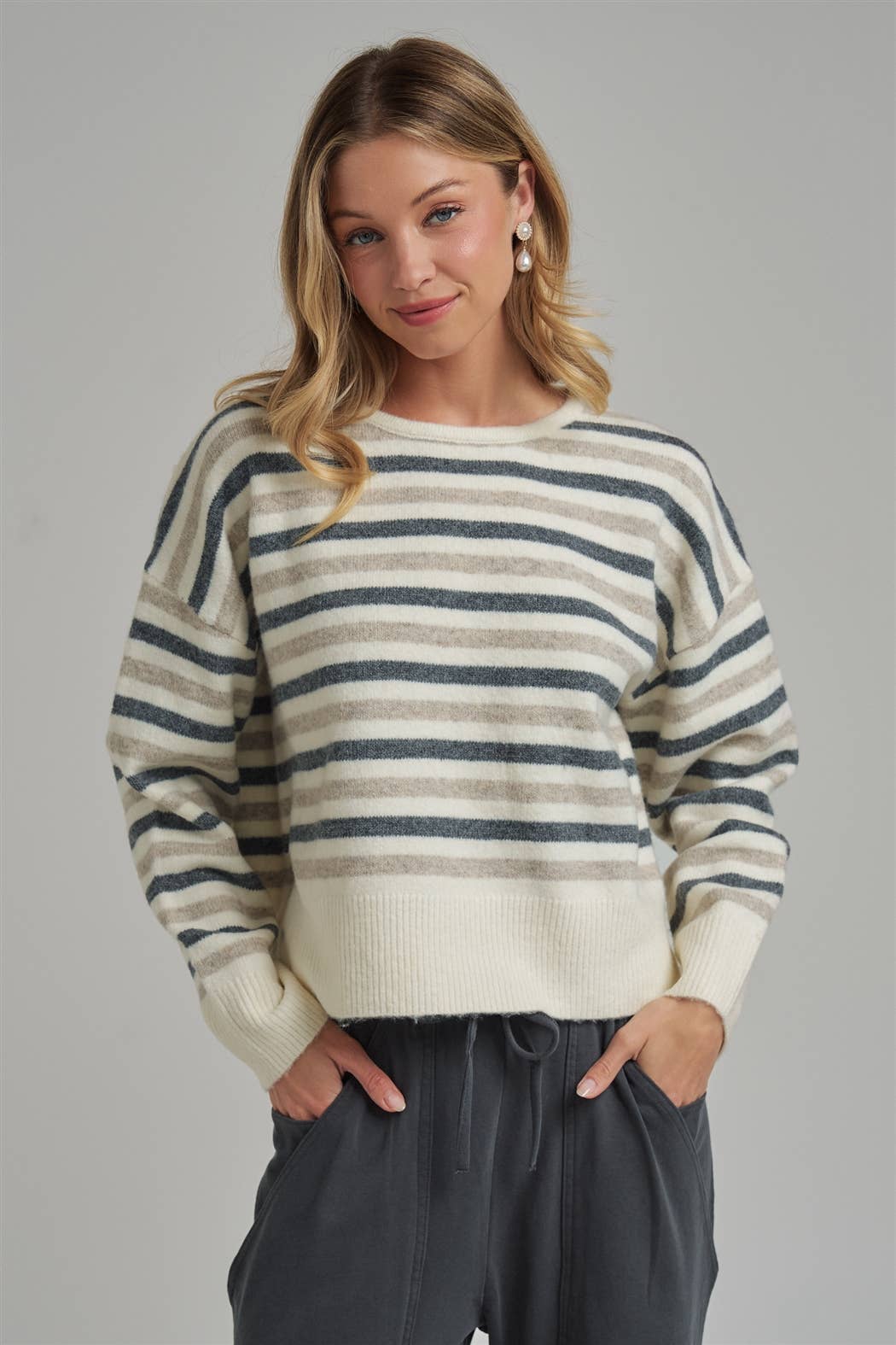 Woman wearing a striped sweater and dark pants against a gray background