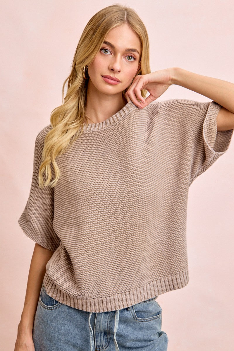 Woman wearing a beige sweater and blue jeans against a pink background