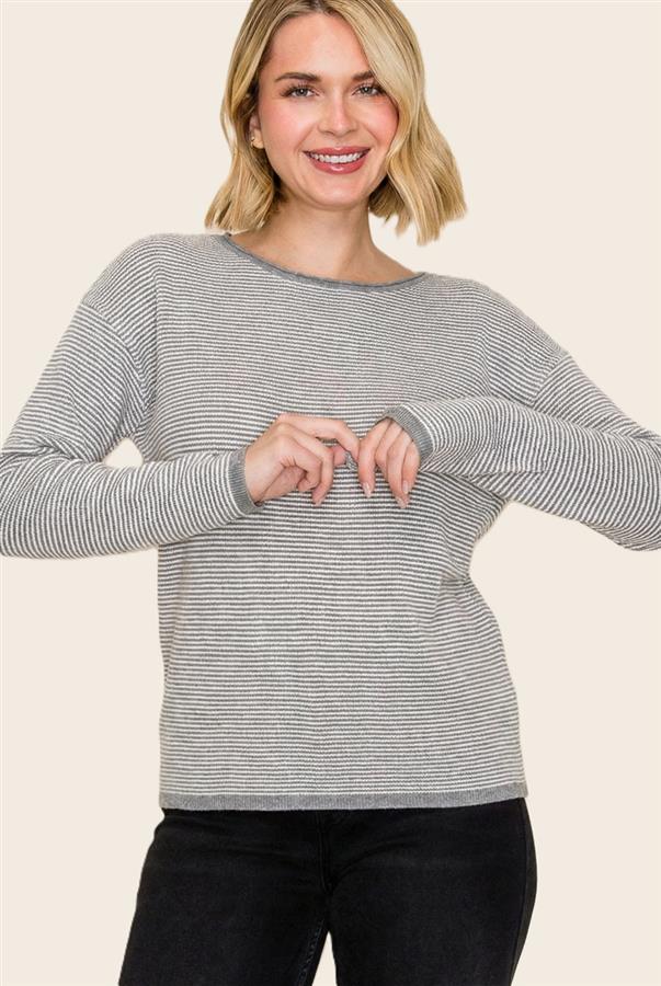 A woman wearing a gray and white horizontally striped long-sleeve knit top, paired with black pants, against a solid light beige background.