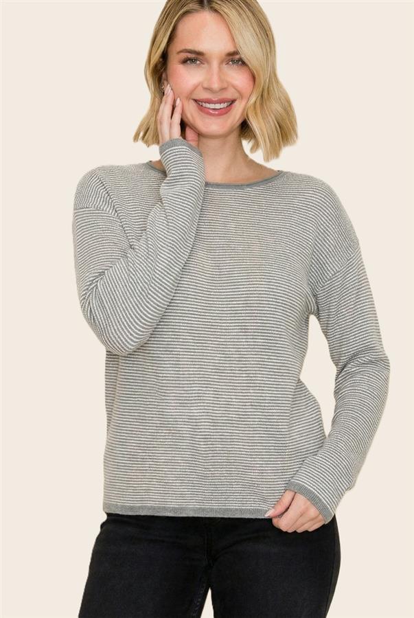A woman wearing a light gray and white horizontally striped long-sleeve knit sweater, paired with black pants, against a solid light beige background.