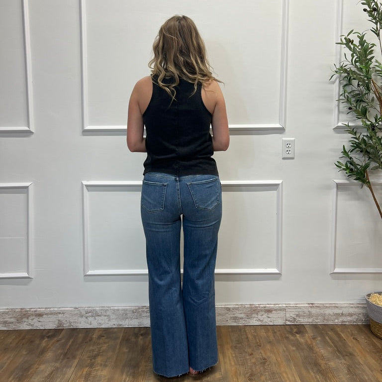 Person wearing blue jeans and a black top standing in a room with white paneled walls and wooden flooring.