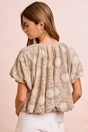 Woman wearing a beige patterned blouse with a pink background