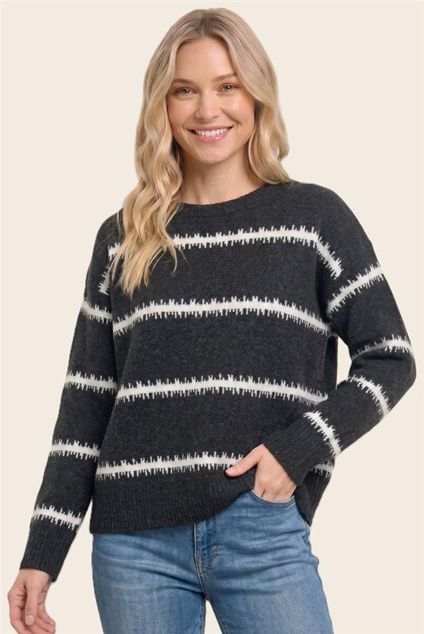 A woman wearing a dark charcoal gray knit sweater with horizontal white textured stripes, paired with blue jeans, against a solid light beige background.