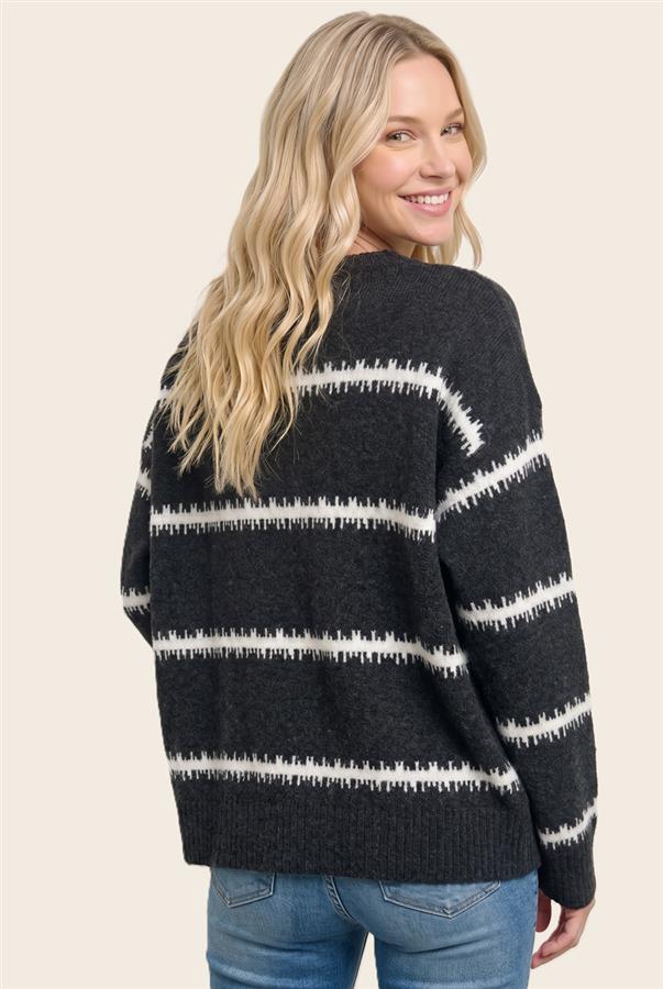 A woman with long blonde hair is shown from the back wearing a dark charcoal gray knit sweater with horizontal white textured stripes, paired with blue jeans, against a solid light beige background.
