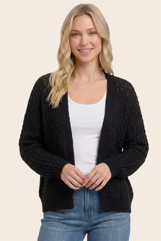 Woman wearing a black cardigan over a white top and blue jeans on a beige background
