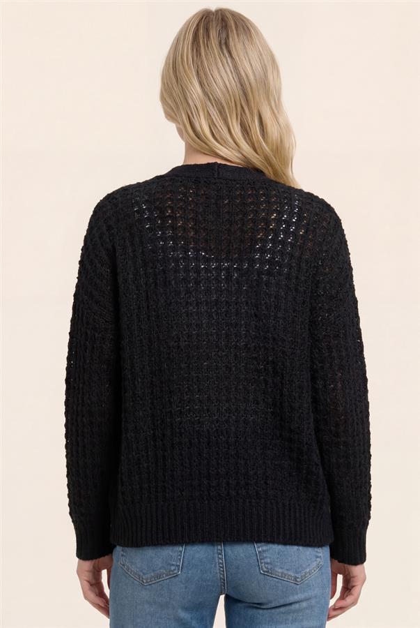 Person wearing a black textured sweater and blue jeans on a beige background