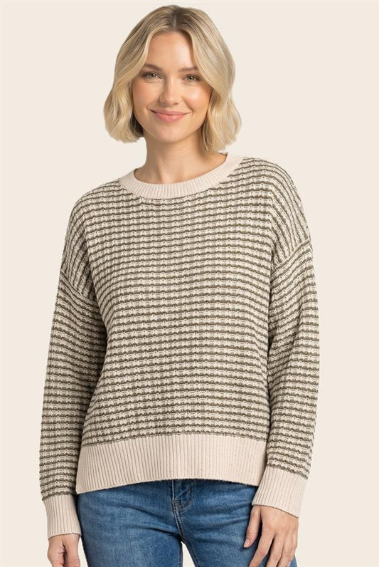 A woman wearing a beige and brown horizontally striped knit sweater with ribbed crew neck, cuffs, and hem, paired with blue jeans, set against a solid light beige background.