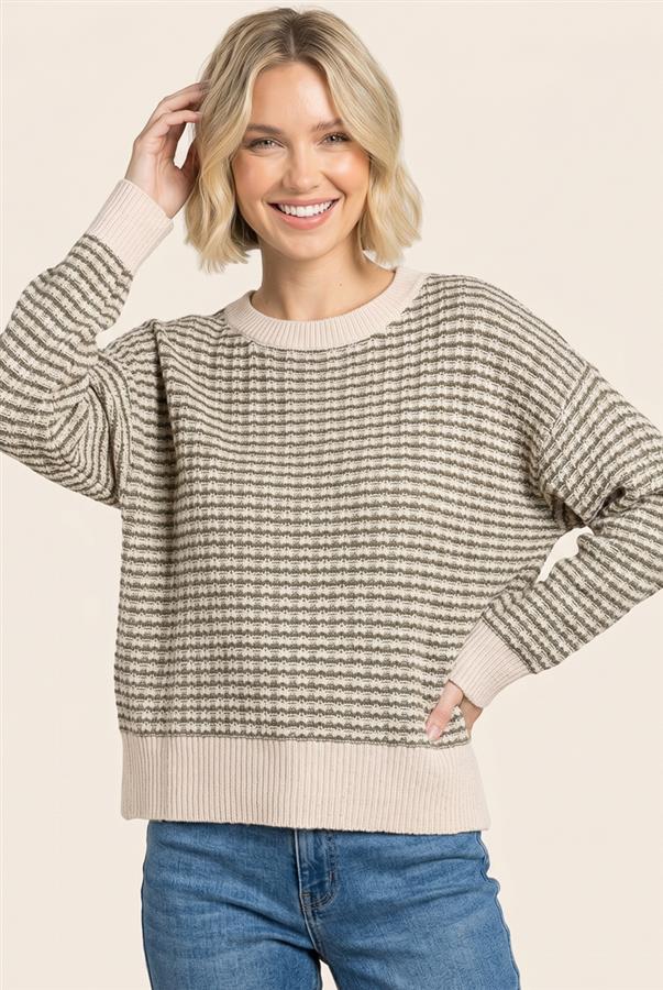 A woman wearing a beige and gray striped knit sweater with ribbed cuffs, collar, and hem, paired with blue jeans, against a solid light beige background.