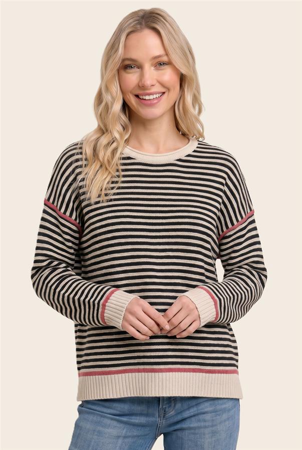 A woman wearing a black and beige horizontally striped crewneck sweater with thin red accent stripes on the shoulders and cuffs, paired with blue jeans, against a solid light beige background.