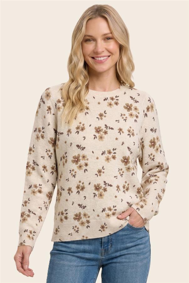 A woman wearing a cream-colored long-sleeve knit sweater with a brown and beige floral pattern, paired with blue jeans, against a solid light beige background.