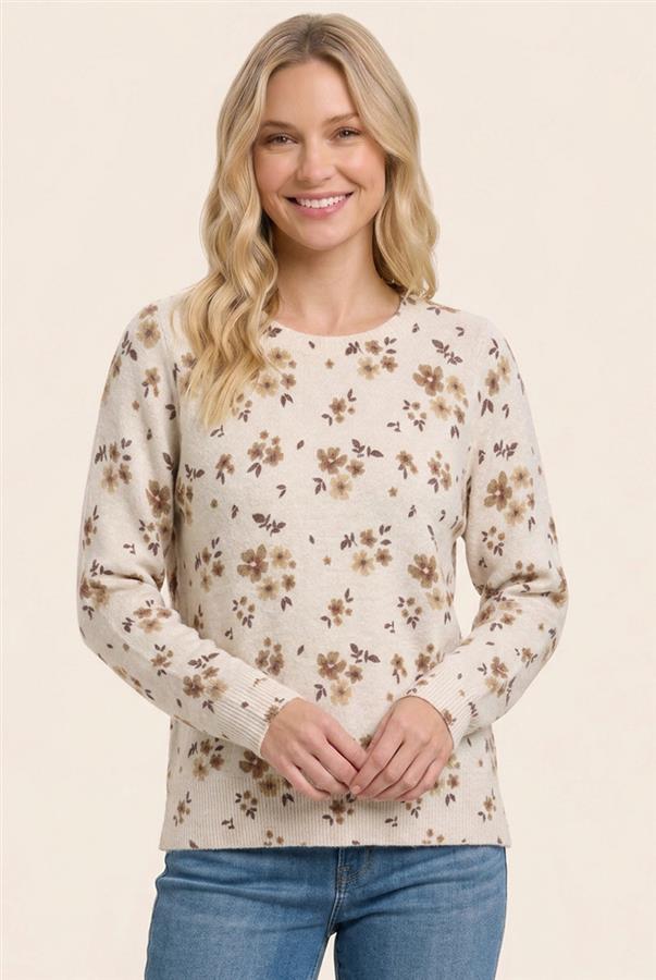 A woman wearing a cream-colored long-sleeve knit sweater with a brown and beige floral pattern, paired with blue jeans, against a solid light beige background.