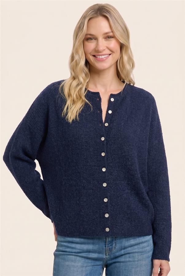 A woman wearing a navy blue knit cardigan sweater with a button-down front and light-colored buttons, paired with blue jeans, against a solid light beige background.