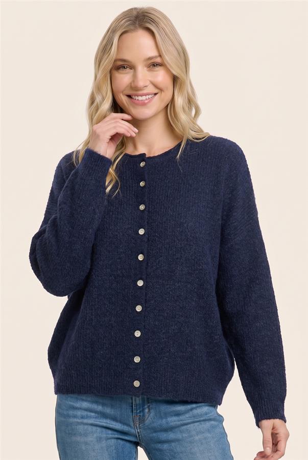 A woman wearing a navy blue knit button-front sweater with light-colored buttons, paired with blue jeans, against a solid beige background.