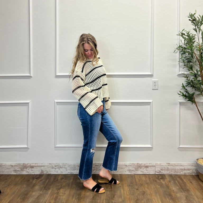 Woman wearing a striped sweater and jeans standing in front of a white paneled wall.