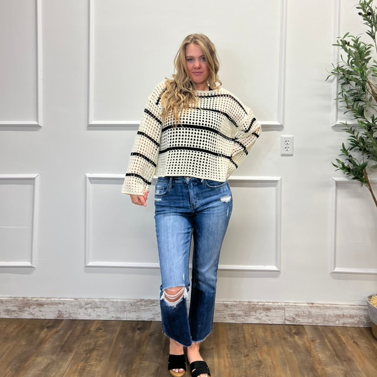Woman wearing a striped sweater and jeans standing in a room with white paneled walls and a plant.