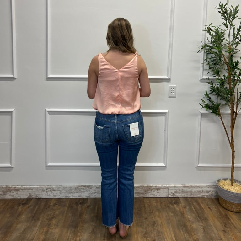 Person wearing a pink top and blue jeans standing in front of a white paneled wall.