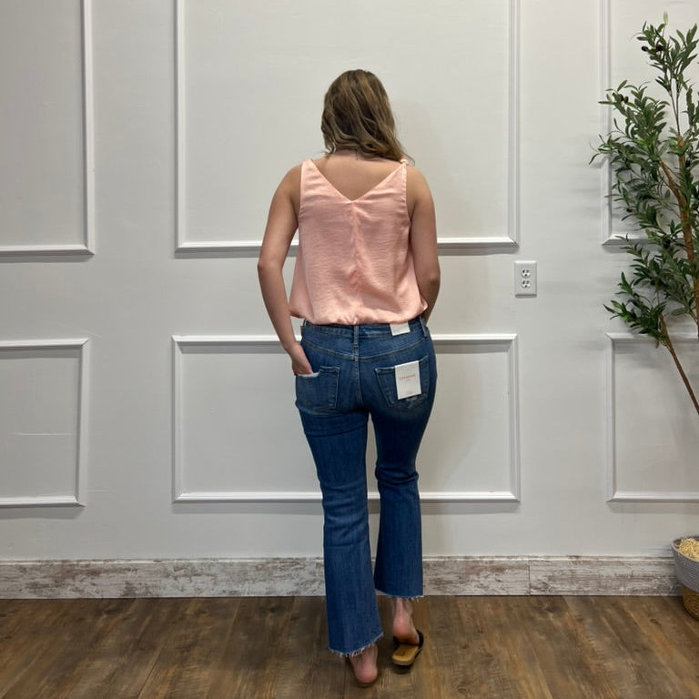 Woman wearing a pink top and blue jeans standing in a room with white paneled walls and a plant.