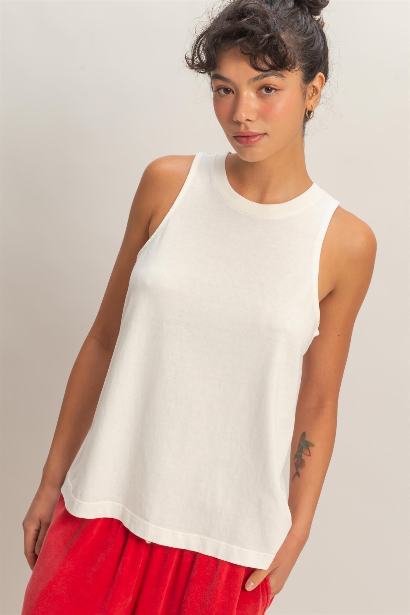 Woman wearing a white sleeveless top and red pants against a plain background