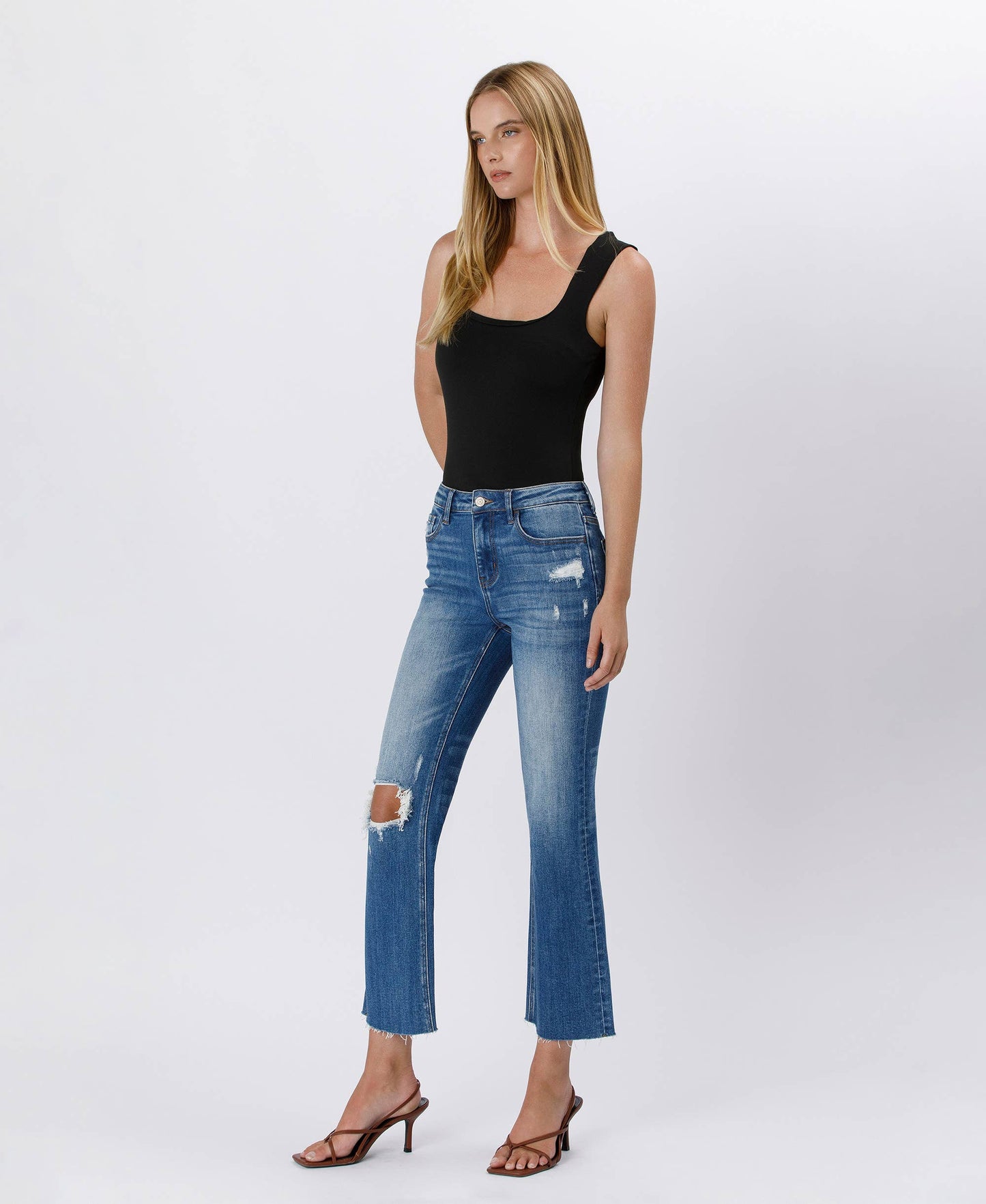 Woman wearing a black tank top and blue jeans on a white background