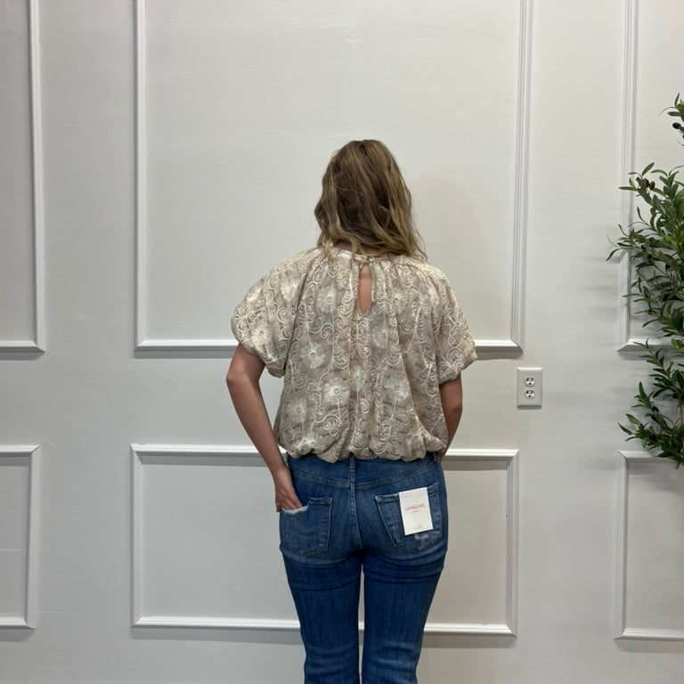 Person wearing a floral blouse and blue jeans standing in front of a white paneled wall.