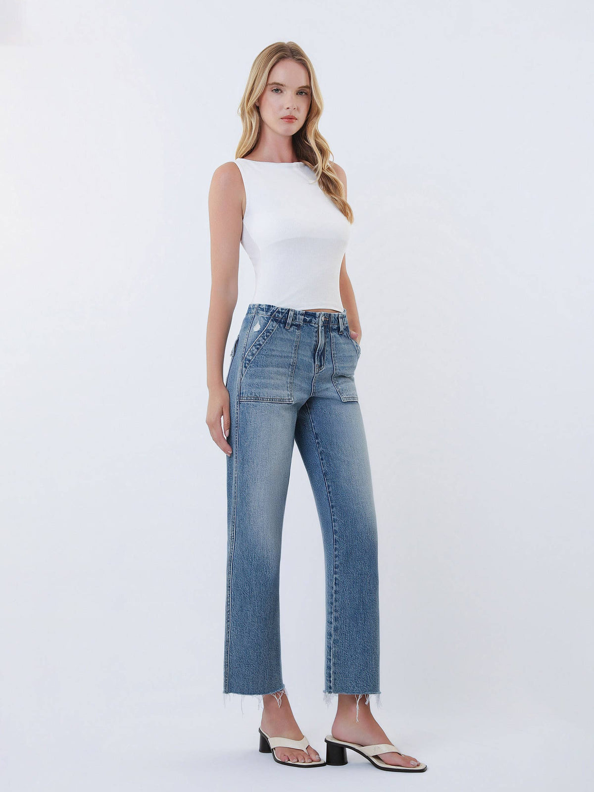 Woman wearing a white sleeveless top and blue jeans on a white background