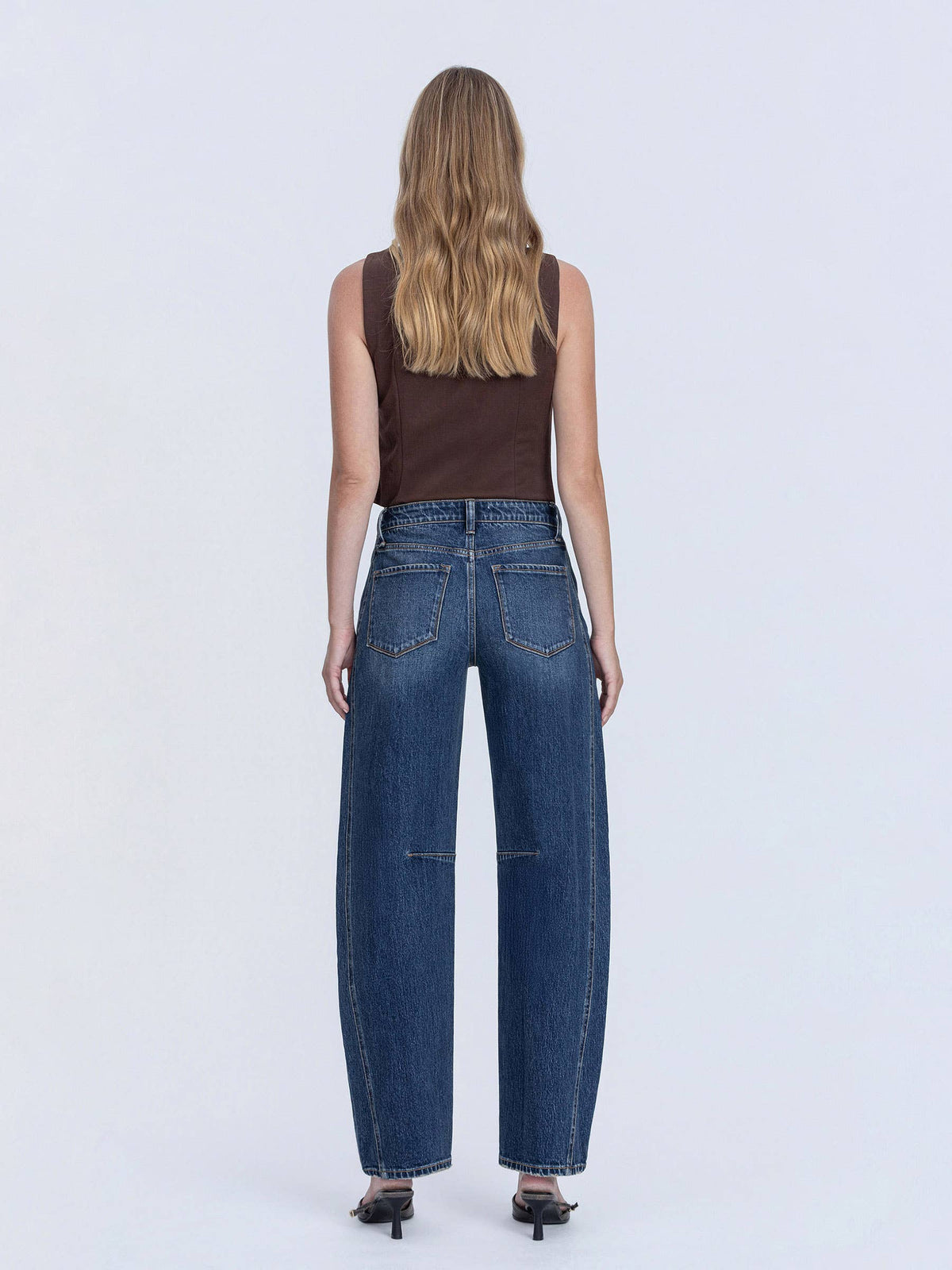 Person wearing blue jeans and a brown top on a white background